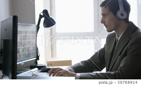 Successful businessman in headphones sitting at his desk, working on a computer by the panoramic 50768914