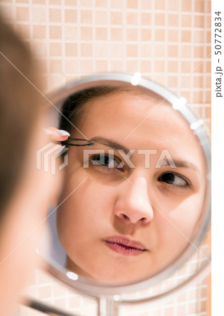 Beautiful woman with tweezers is plucking eyebrows Beautiful woman with tweezers is plucking eyebrows 50772834
