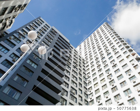 View from the ground on roof tops of modern multistored living building against blue sky and bright 50775638