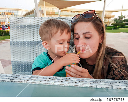 Funny portrait of young mother with toddler boy drinking orange juice from two straw at beach cafe 50778753