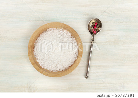 A bowl of sea salt and a spoon with pepper, shot from above on a white wooden background with copy 50787391
