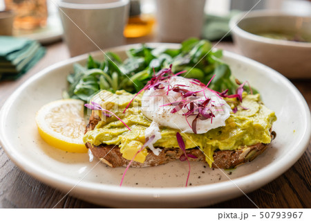 Morning in cafe, oak table. Healthy breakfast with wholemeal bread toast with avocado, poached egg 50793967