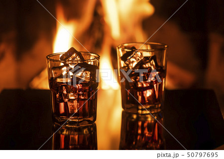 Glass of whiskey with ice near the fireplace Glass of whiskey with ice near the fireplace 50797695