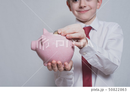 Smiling boy puts a coin in a pink piggy bank. 50822863