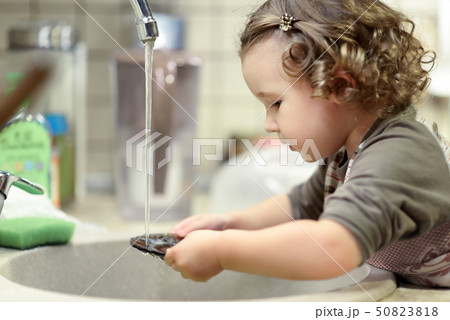 Little child is washing dishes in kitchen Little child is washing dishes in kitchen 50823818