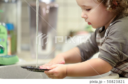 Little child is washing dishes in kitchen Little child is washing dishes in kitchen 50823821