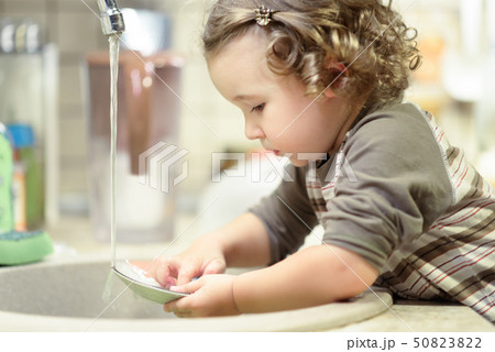 Little child is washing dishes in kitchen Little child is washing dishes in kitchen 50823822