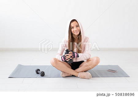 Healthy lifestyle, people and sport concept - Smiling woman sitting on yoga mat and drinking water 50838696