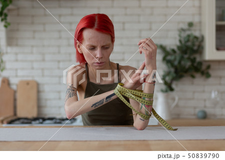 Skinny red-haired woman taking tape measure off her hands 50839790