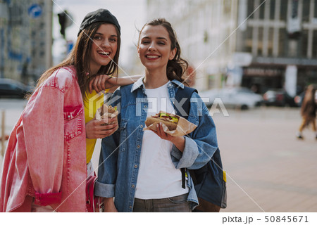 Cheerful girls walking around eating hot dogs Cheerful girls walking around eating hot dogs 50845671