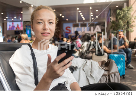 Female traveler reading on her cell phone while waiting to board a plane at departure gates at 50854731