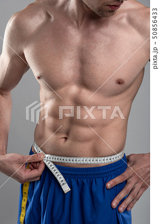 Strong athletic young man with perfect body measuring his waist 50856433