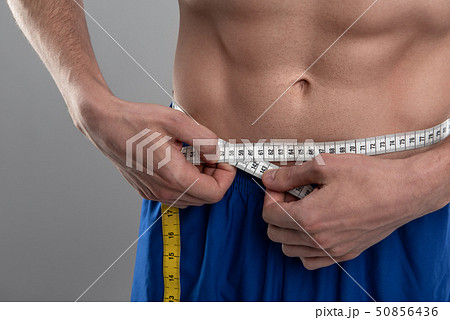 Young man with perfect abs measuring his waist 50856436
