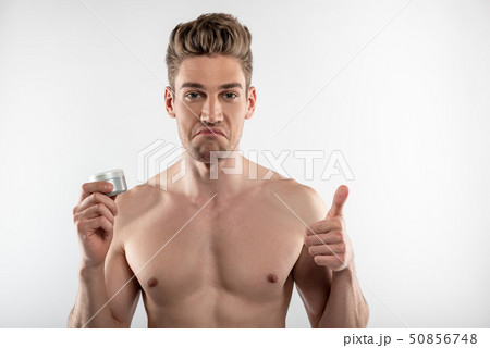 Handsome young man holding jar of cosmetic cream and showing thumbs up 50856748