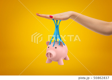 Pink piggy bank stuck to female hand with blue sticky slime on yellow background 50862837