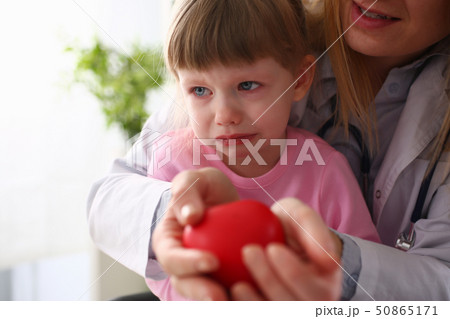 Scared little baby girl visiting doctor holding in hands red toy heart 50865171