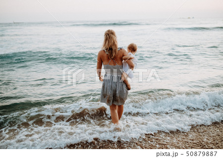 Rear view of young mother with a toddler girl walking in sea on summer holiday. 50879887