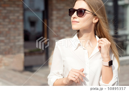 Portrait of a successful happy business woman in a white shirt and sunglasses. Smart watch on a hand Portrait of a successful happy business woman in a white shirt and sunglasses. Smart watch on a hand 50895357