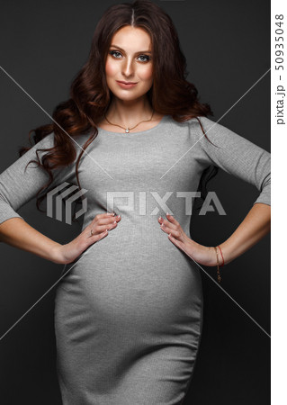 Beautiful pregnant woman in a gray dress, with a classic make up and curls. Beauty face. 50935048