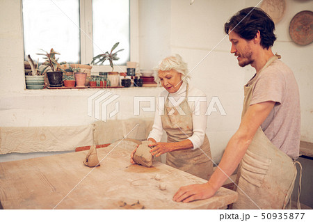 Positive aged woman showing how to work with clay Positive aged woman showing how to work with clay 50935877