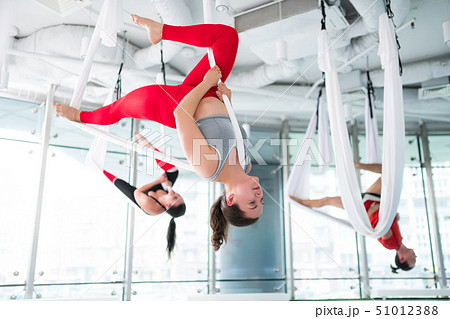 Dark-haired trainer in red leggings showing nice aerial yoga pose Dark-haired trainer in red leggings showing nice aerial yoga pose 51012388