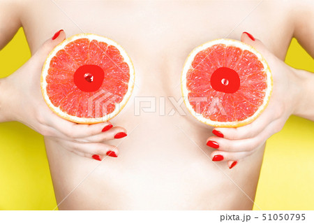 Sexy young woman holding grapefruits near her breasts on color background. Erotic concept 51050795