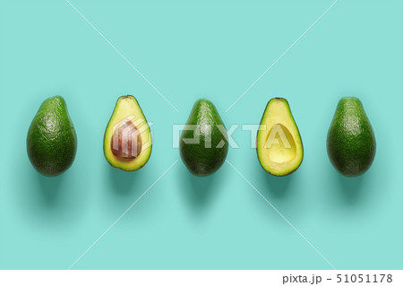 Row of fresh wholes and halves of organic avocado with kernels in center on blue backgrond. Top view 51051178
