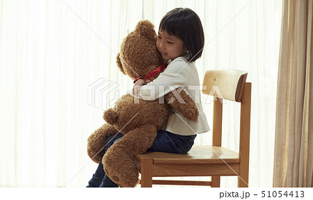 椅子に腰掛け大きな熊と遊ぶ女の子の写真素材