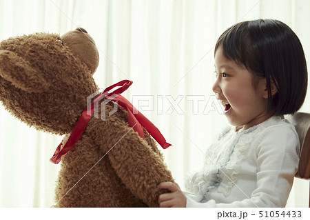 椅子に腰掛け大きな熊と遊ぶ女の子の写真素材