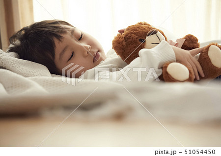 ベッドで小さなクマと寝る女の子の写真素材