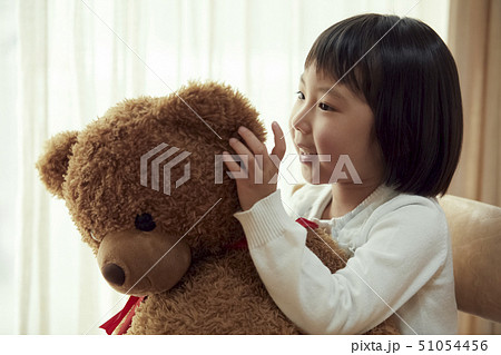 椅子に腰掛け大きな熊と遊ぶ女の子の写真素材