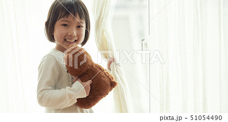 小さなクマを持ち窓際に立つ女の子 51054490