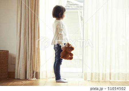 小さなクマを持ち窓際に立つ女の子 51054502