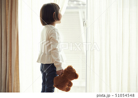 小さなクマを持ち窓際に立つ女の子 51054548