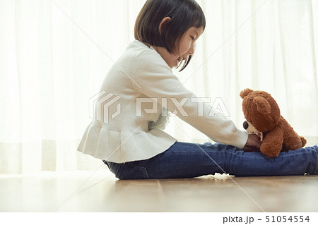 床に座り小さなクマと遊ぶ女の子の写真素材