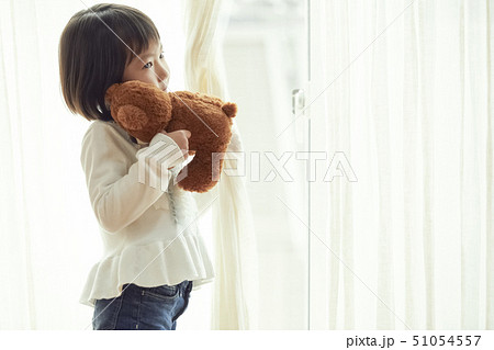 小さなクマを持ち窓際に立つ女の子 51054557