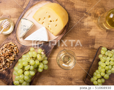 Flat lay top view of various cheeses next to fresh grapes, glass of wine on a wooden table 51068930