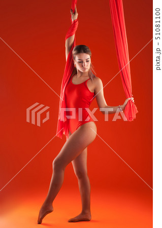 A young blonde girl with long hair in a red suit performs gymnastic and exercises on silk. A young blonde girl with long hair in a red suit performs gymnastic and exercises on silk. 51081100