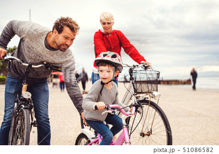 Young family and small daughter with bicycles outdoors on beach. Young family and small daughter with bicycles outdoors on beach. 51086582