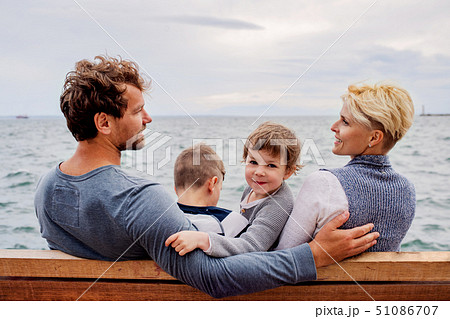 Young family with two small children sitting on bench outdoors on beach. Young family with two small children sitting on bench outdoors on beach. 51086707