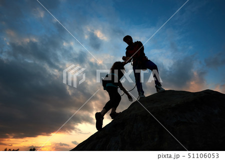Young couple man and woman climbing on boulder. Helping hand. Silhouettes on sunset background. 51106053