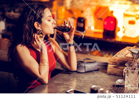 Woman in red dress sitting at the bar counter and drinking alone Woman in red dress sitting at the bar counter and drinking alone 51124111