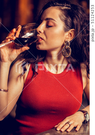 Close up of curly woman wearing red dress drinking red wine 51124253