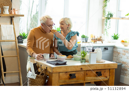 Glowing wife tenderly feeding up the old spouse with croissant 51132894