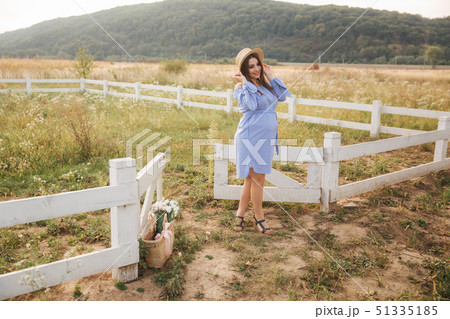 Pregnant woman in nature try on knitted hat. Background of field and white fance near the farm Pregnant woman in nature try on knitted hat. Background of field and white fance near the farm 51335185