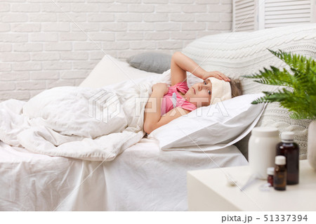 Sick little girl lying in bed with thermometer Sick little girl lying in bed with thermometer 51337394