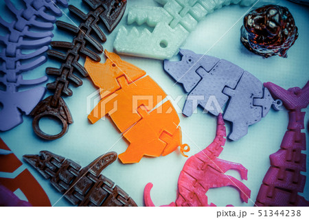 Many bright multi-colored objects printed on 3d printer lie on flat surface 51344238
