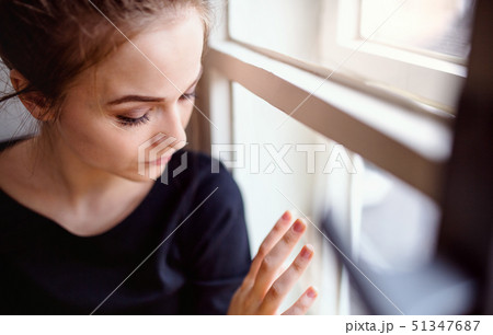 A close-up of young sad female student sitting on window sill. A close-up of young sad female student sitting on window sill. 51347687