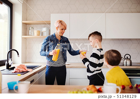 A young woman with two children drinking juice in a kitchen. A young woman with two children drinking juice in a kitchen. 51348129