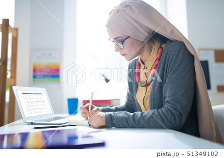 Muslim teacher wearing glasses making notes after work Muslim teacher wearing glasses making notes after work 51349102